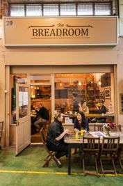Exterior of 'the BREADROOM' cafe with indoor and outdoor seating, people enjoying coffee and conversation.