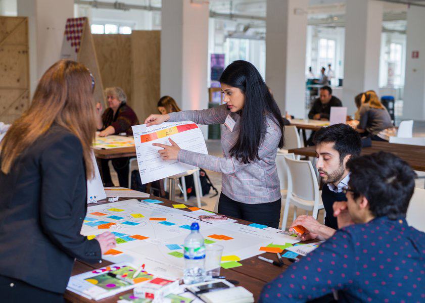 People collaborating at a table, reviewing a diagram or chart with sticky notes during a workshop.