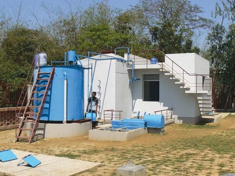 An outdoor water treatment facility featuring large blue tanks, interconnected pipes, and a small white building with external stairs.