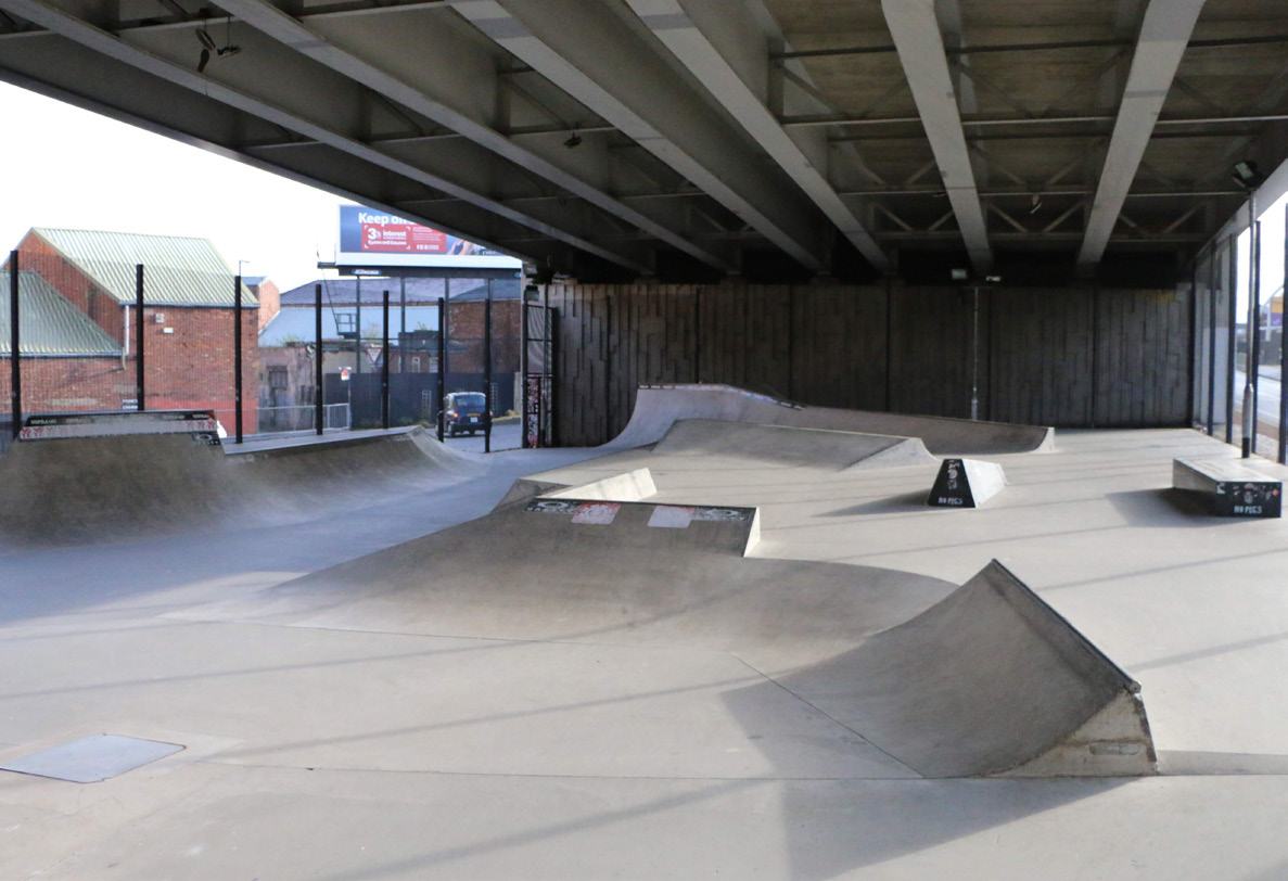 An empty concrete skate park featuring various ramps and obstacles, situated under an elevated bridge.