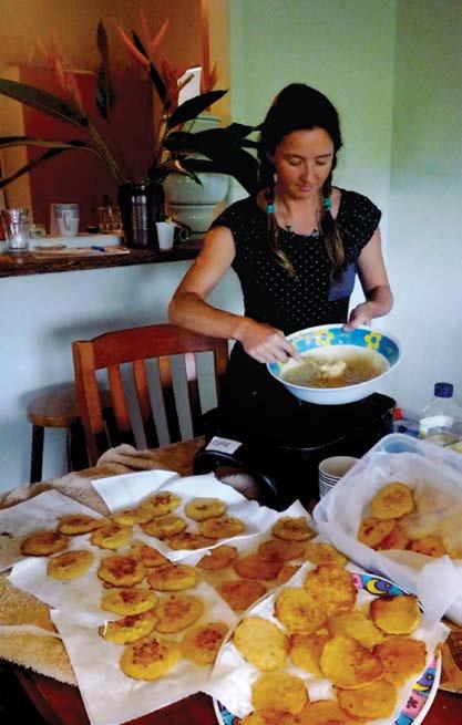 Woman preparing food in a kitchen, holding a bowl over a pot, surrounded by many small fried items on a table.