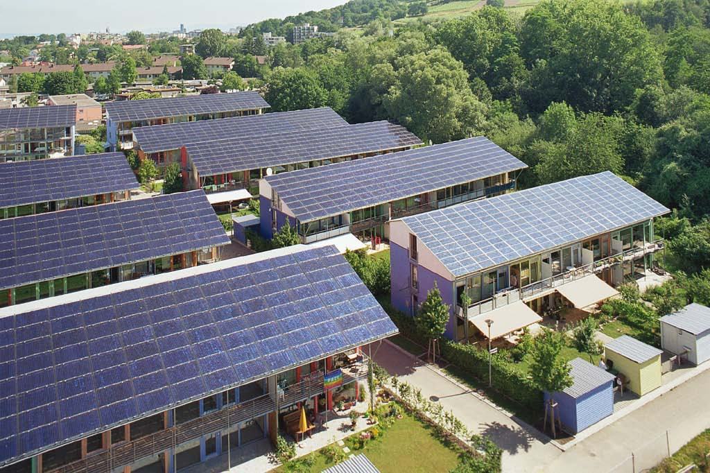 Aerial view of a housing complex where multiple residential buildings feature roofs completely covered with solar panels.