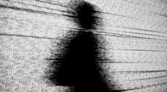A blurry, pixelated silhouette of a person standing against a grainy, static background with horizontal lines, suggesting digital presence or anonymity.