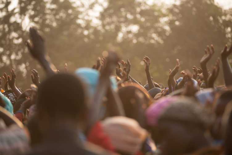A large crowd of people with many hands raised in the air, suggesting collective participation or emotion at an event.