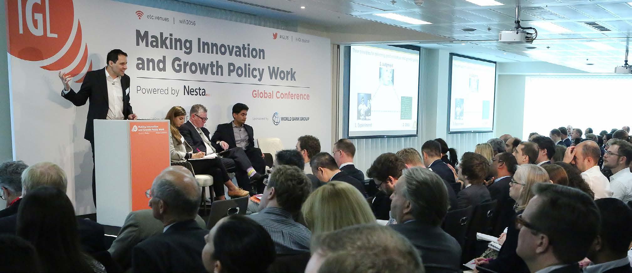 A speaker at a podium addressing a large audience in a conference room, with a screen displaying "Making Innovation and Growth Policy Work".