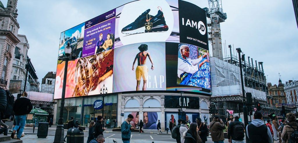 Piccadilly Circus in London with large digital billboards displaying advertisements, surrounded by people walking in the street.