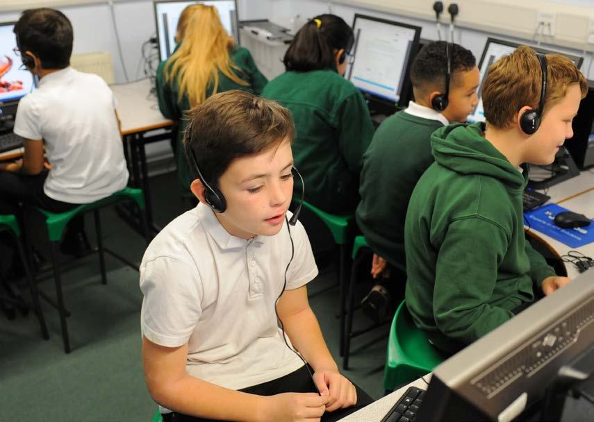 Students wearing headphones and using computers in a classroom setting, engaged in learning activities.