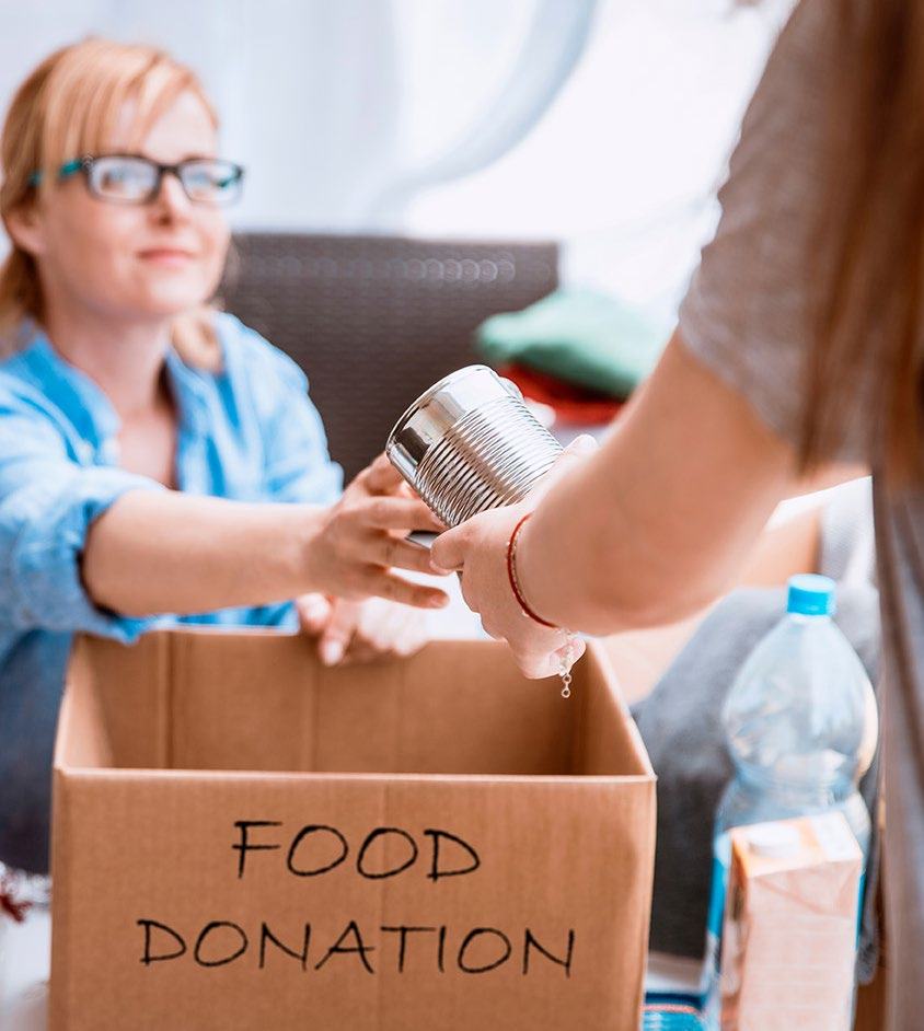 A person hands a canned food item into a box labeled "FOOD DONATION" during a charity drive.