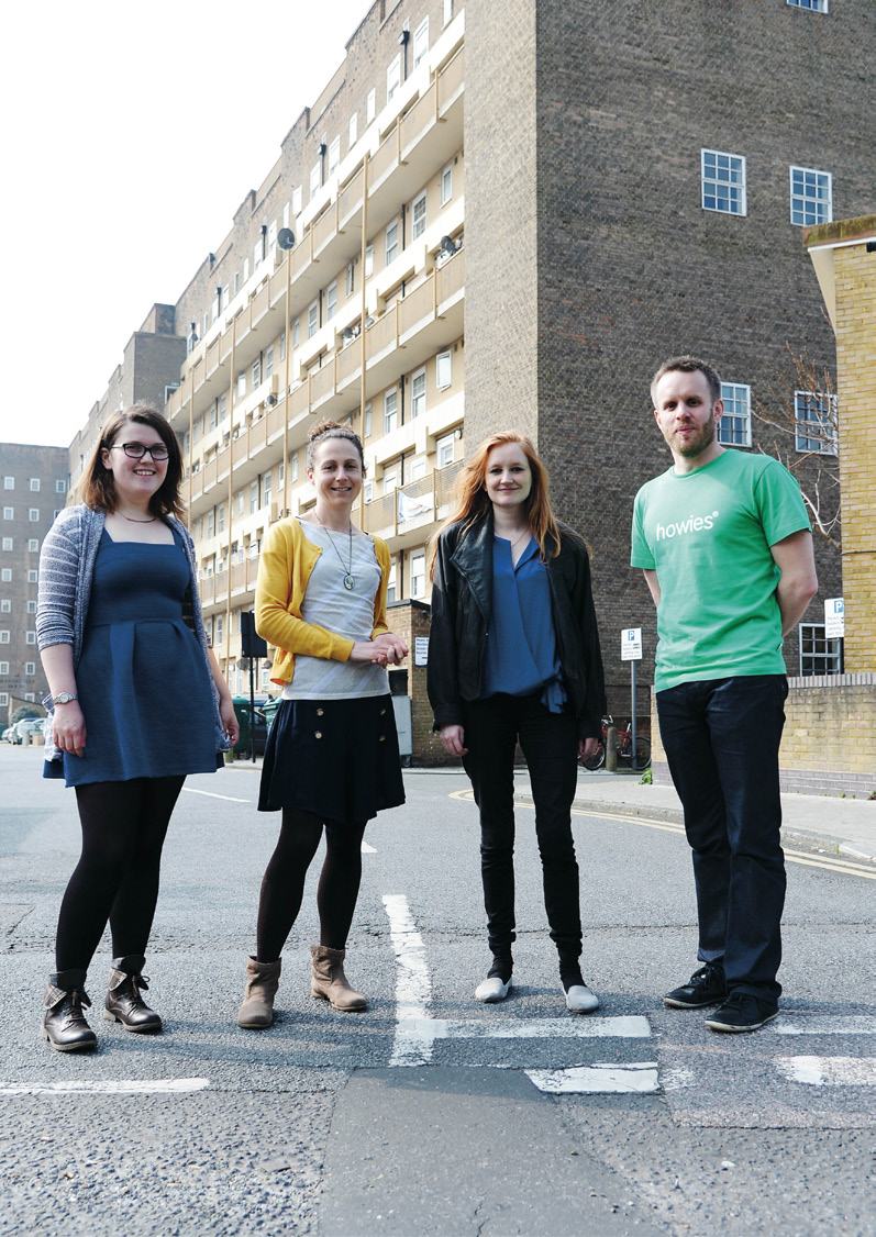 Four people, two women and two men, standing on a street in front of an apartment building, likely a team photo.