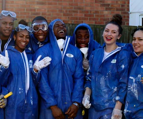 Group of young people in blue coveralls and goggles, laughing, with paint on their clothes.