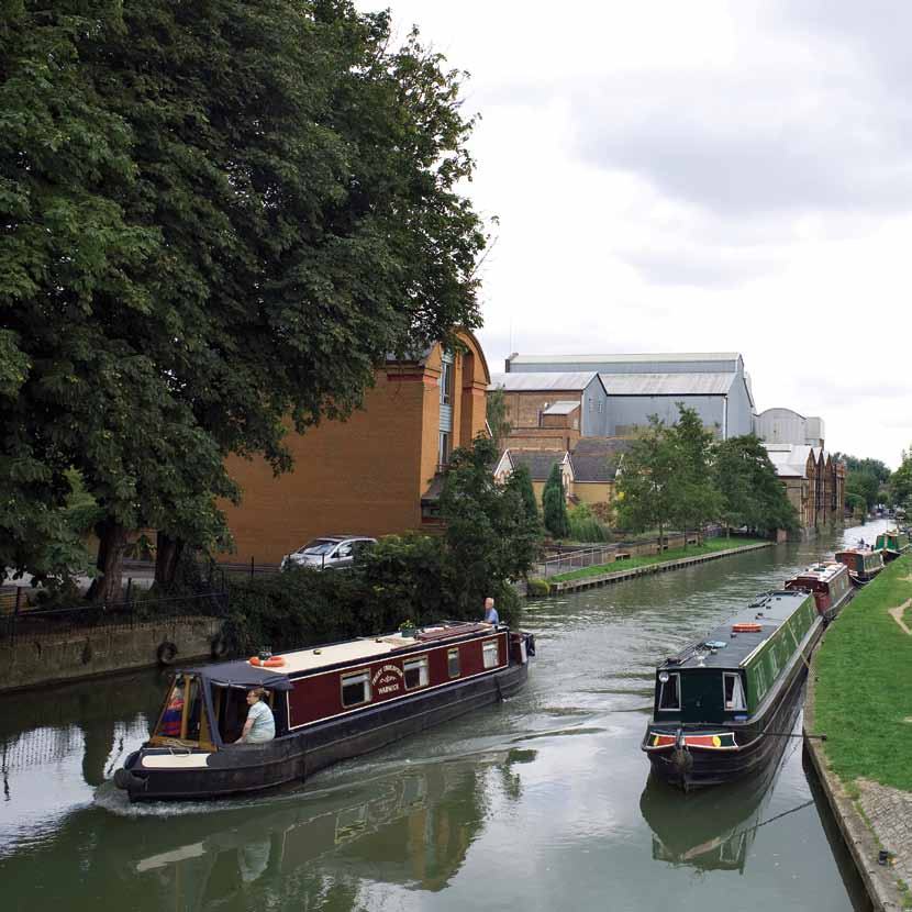 Several colorful narrowboats navigating a canal, with buildings and trees lining the banks.