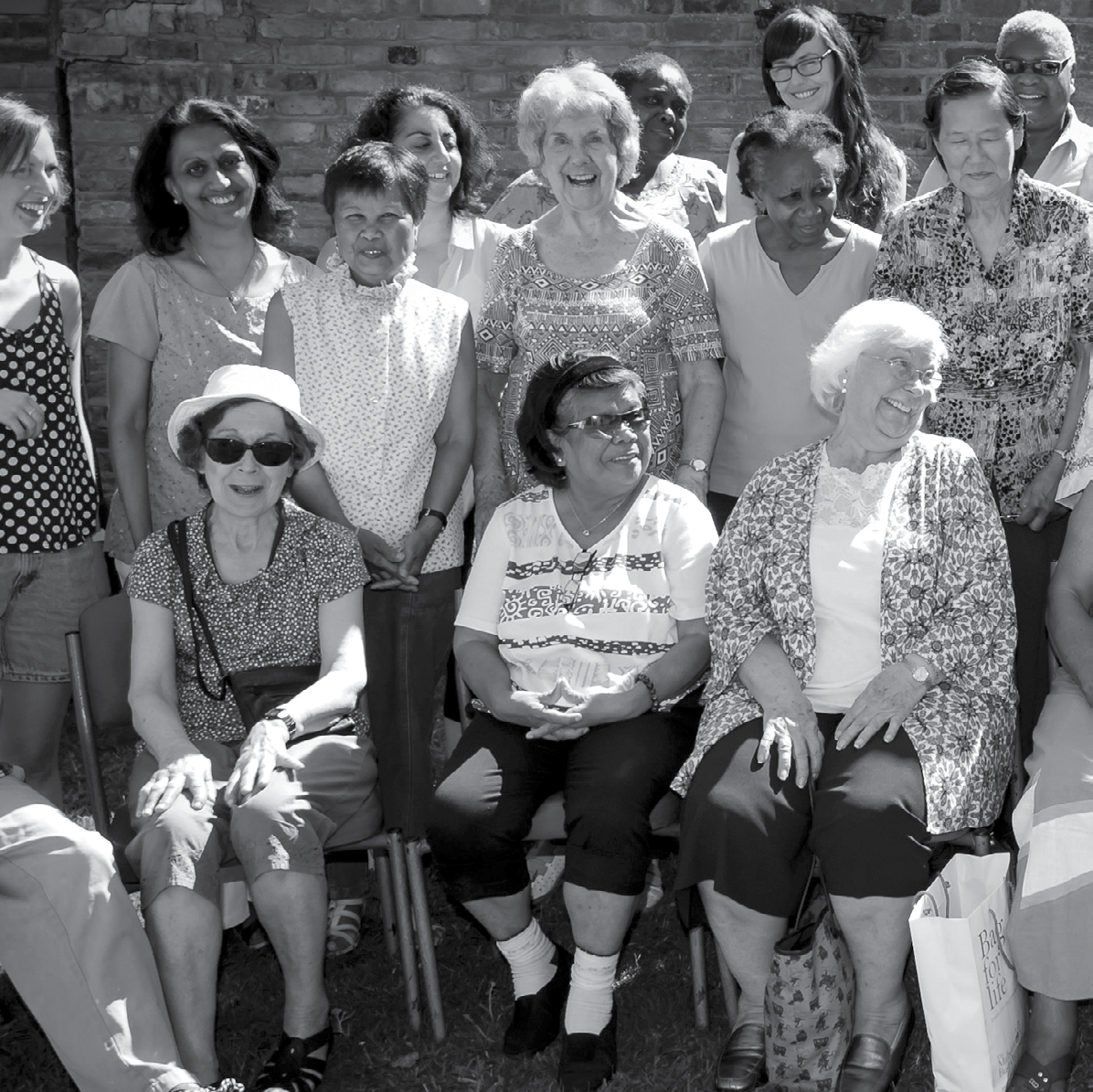Black and white group photo of diverse community members, mostly women of varying ages, smiling outdoors.