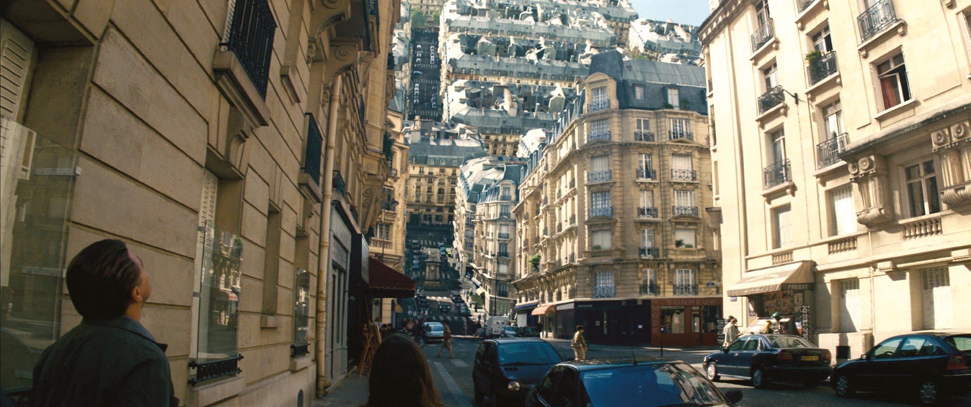 A city street scene with classic European architecture, where the background buildings curve upwards and fold over, creating a surreal, inverted cityscape.