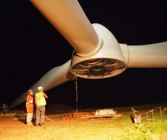 Workers in safety gear inspect a large wind turbine blade being installed at night.
