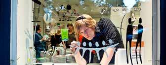 A person meticulously applying paint or decals to a storefront window, with the interior of the shop visible in the background.