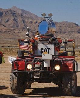 Red all-terrain vehicle equipped with a large laser device and sensors in a desert landscape.