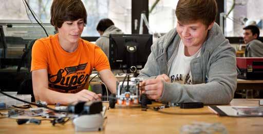 Two young men assembling a small robot or mechanical device at a table, smiling as they work.