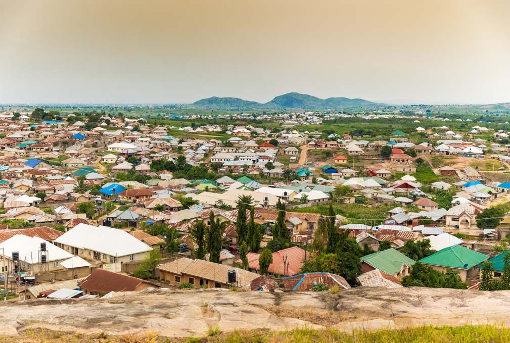 Elevated panoramic view of a densely packed town with many houses and colorful roofs, stretching towards distant hills under a cloudy sky.
