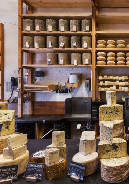 Interior of a cheese shop, showing shelves stocked with various cheeses and a counter display with blue cheeses and price tags.