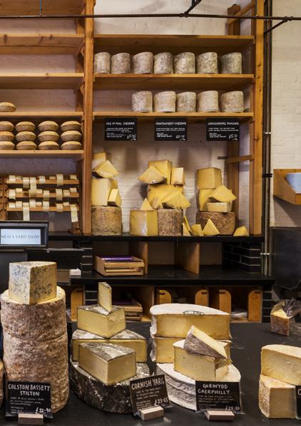 Cheese shop interior with a wide selection of cheeses on display, including labelled cheddar varieties on shelves and counters.