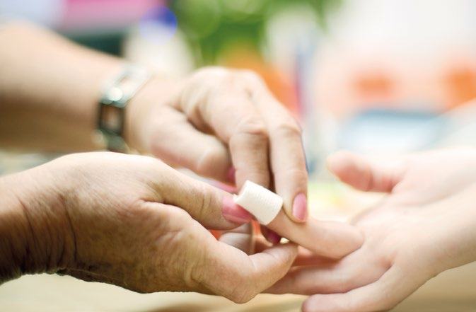 Close-up of an older hand carefully placing a small bandage on the finger of a younger hand, suggesting first aid or medical care.
