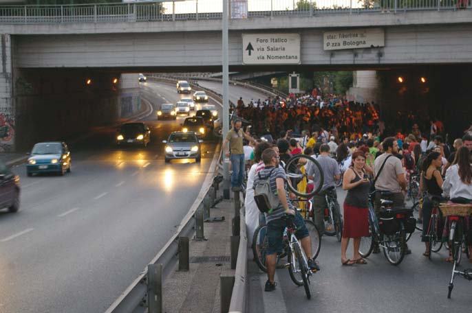 Street scene with an underpass, cars, and a large group of people with bicycles gathered on the side of the road.