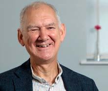 Headshot of an older man smiling, wearing a blue blazer over a checkered shirt.