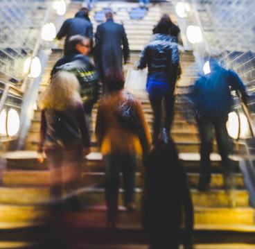 Blurred image of several people ascending a brightly lit indoor staircase.