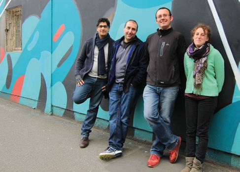 Four people, three men and one woman, standing outdoors against a graffiti-covered wall, likely a team photo.
