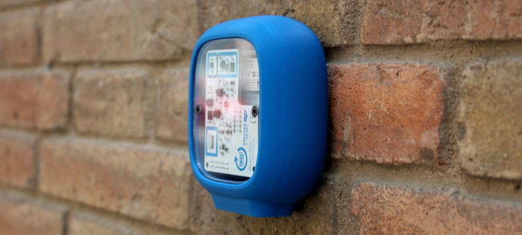A blue, wall-mounted technical device with a clear cover revealing its internal electronic components and circuitry.