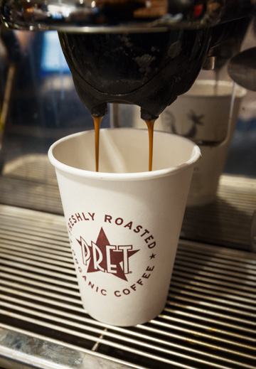 Close-up of espresso coffee being brewed from a machine into a Pret A Manger branded paper cup.