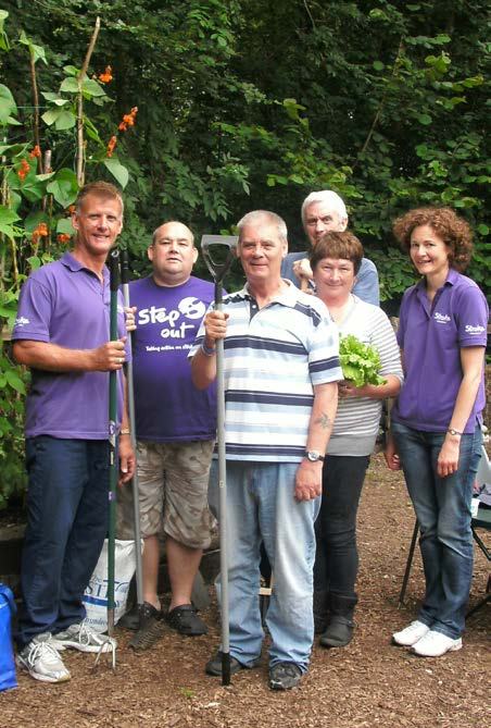 Group of six people in a garden, holding gardening tools, some wearing purple shirts, suggesting a community gardening or outdoor activity.
