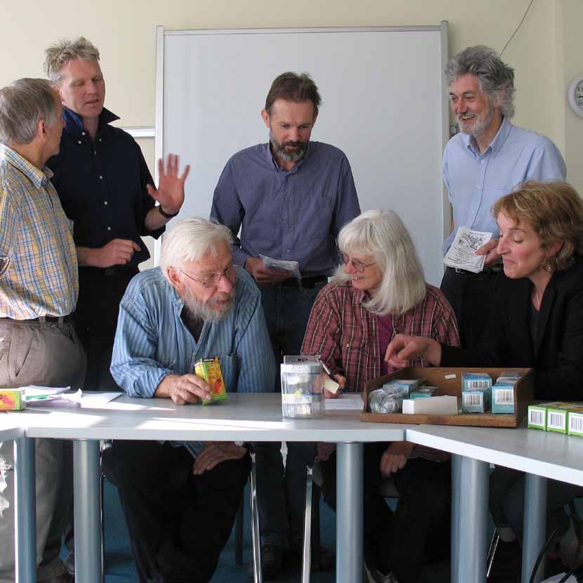 A group of seven adults in a meeting, gathered around a table with boxes, engaged in discussion.