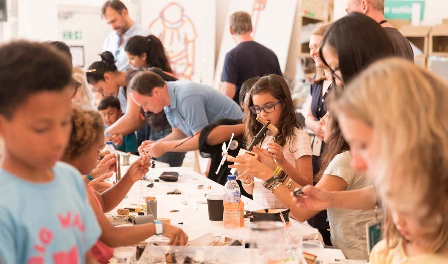 Children and adults participate in a hands-on workshop, working on small projects at tables.