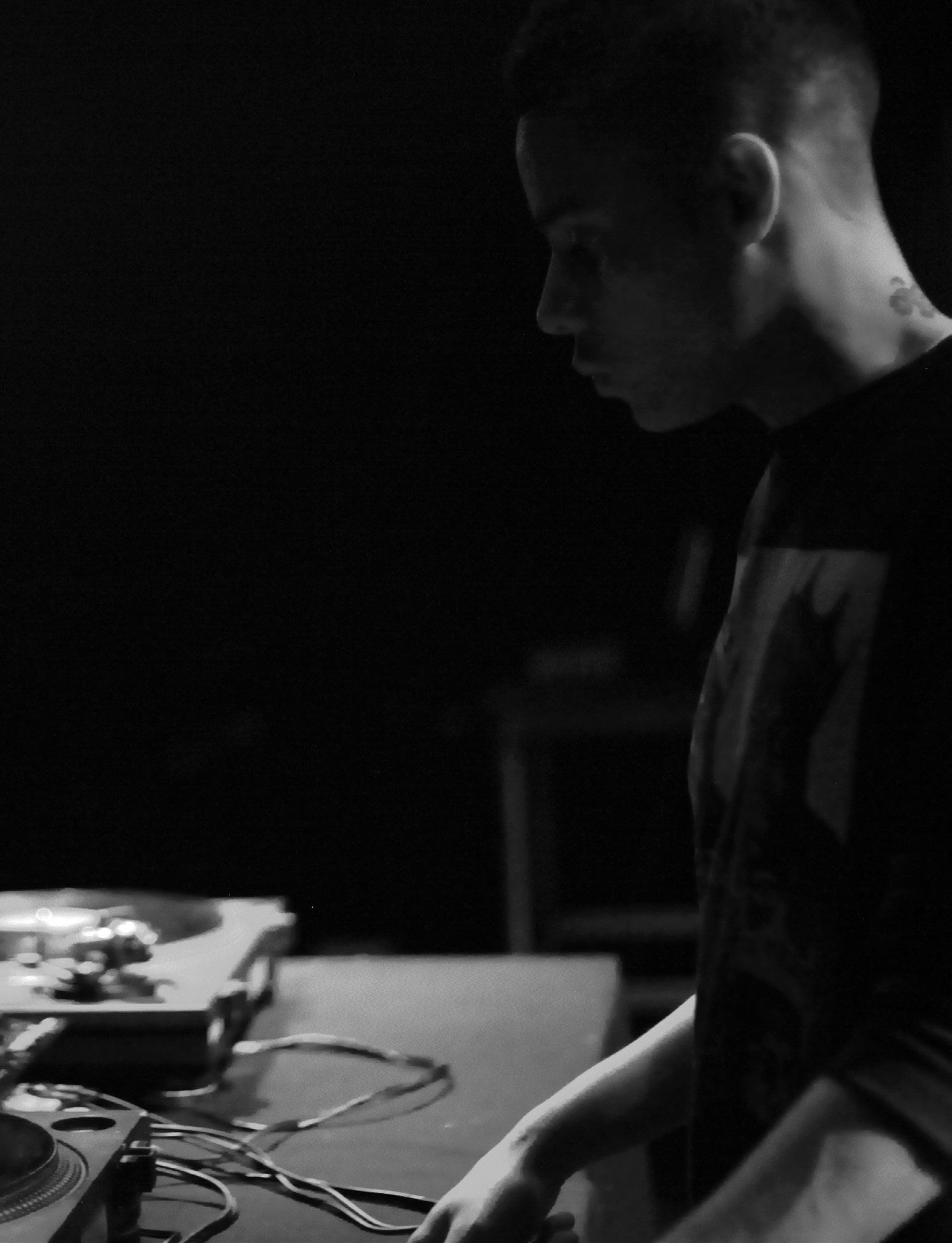 Black and white side profile of a person looking at and interacting with DJ turntables and mixer.
