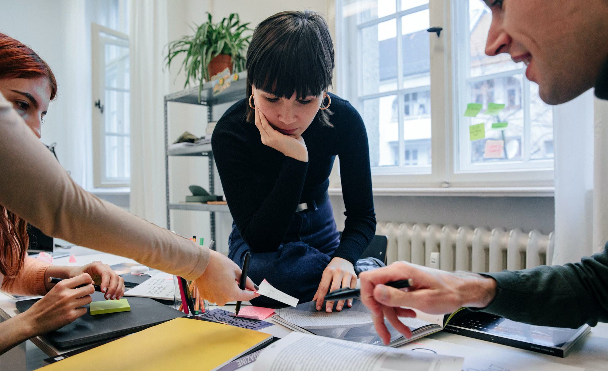Four people collaborating, reviewing documents and a laptop screen at a table.