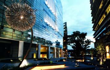 Modern glass building exterior with a large, illuminated dandelion-shaped sculpture in the foreground at dusk.