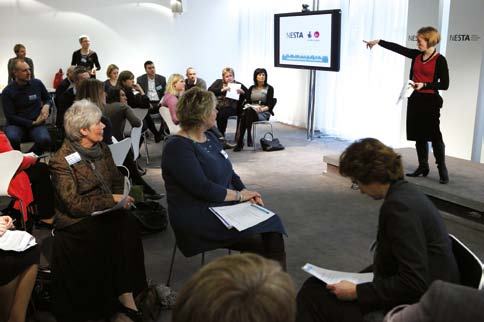 A presenter pointing at a screen displaying a bar chart or graph to an audience.