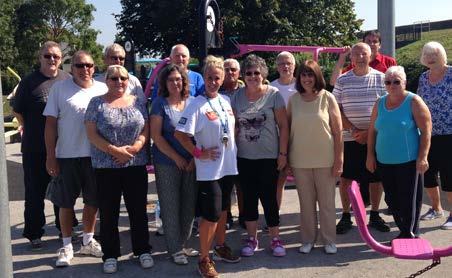 Group of adults standing outdoors in front of exercise equipment, possibly an outdoor fitness class or community exercise group.